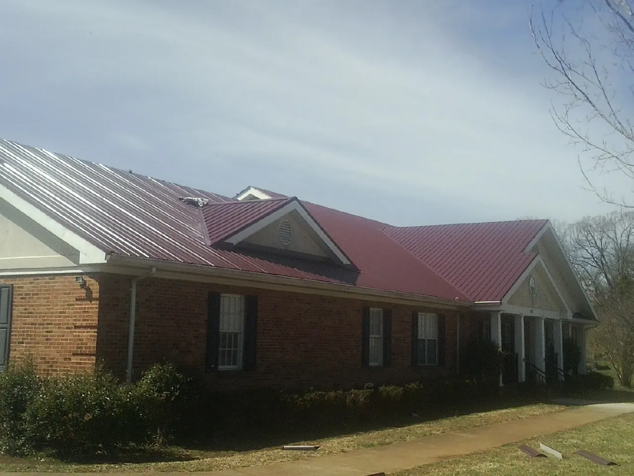 Red metal roof with gabled entries on a long brick building, from a Hail Damage Roof Repair job in East Meadow