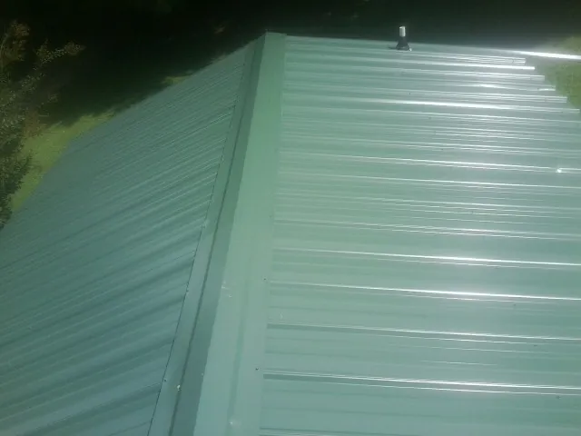 New green metal panels meeting at the ridge of a roof — Flat Roof Repair work by our crew in East Meadow