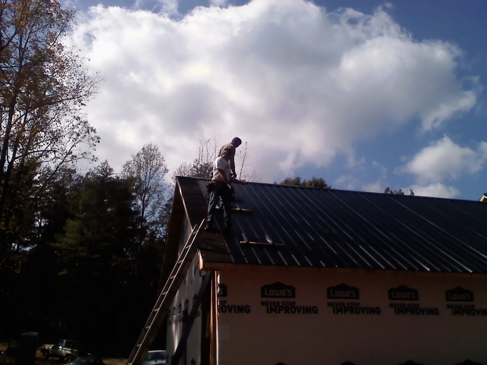 Roofer fastening dark metal panels high against a cloudy sky, from a Roof Inspection job in East Meadow