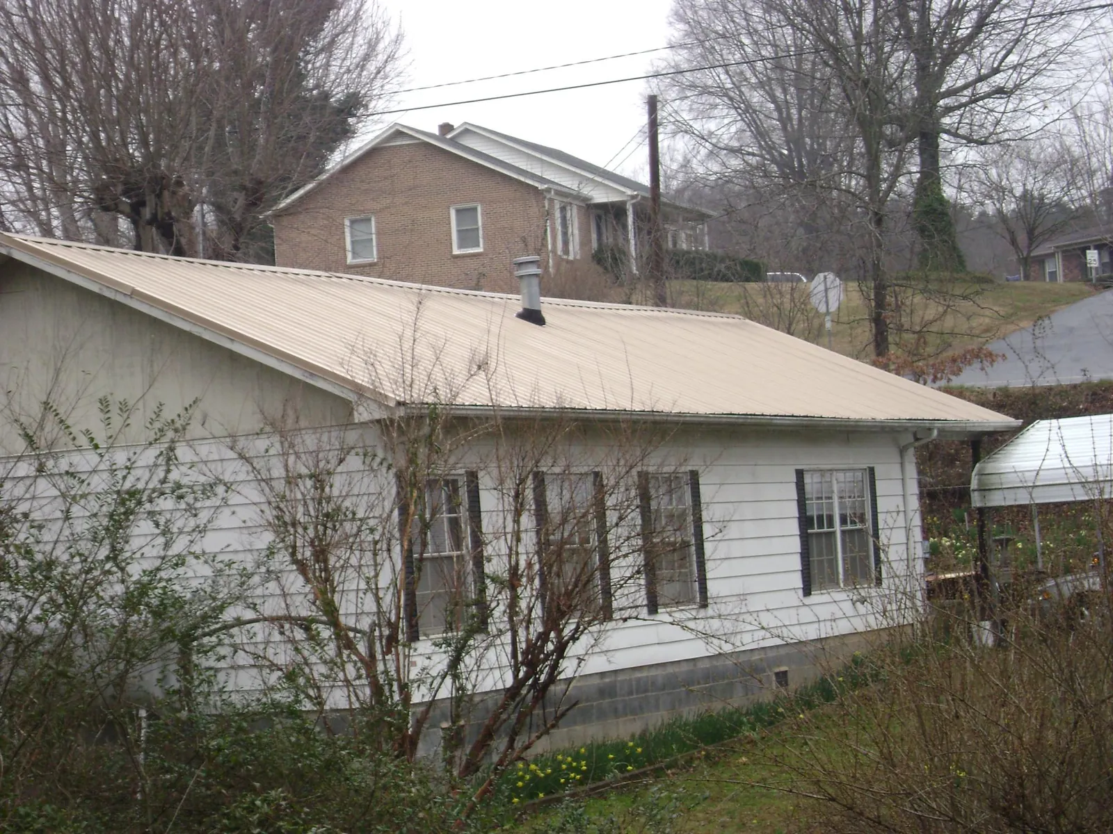 Tan metal roof on a white sided house set into a hillside — Commercial Roofing by Roofing Brothers in East Meadow