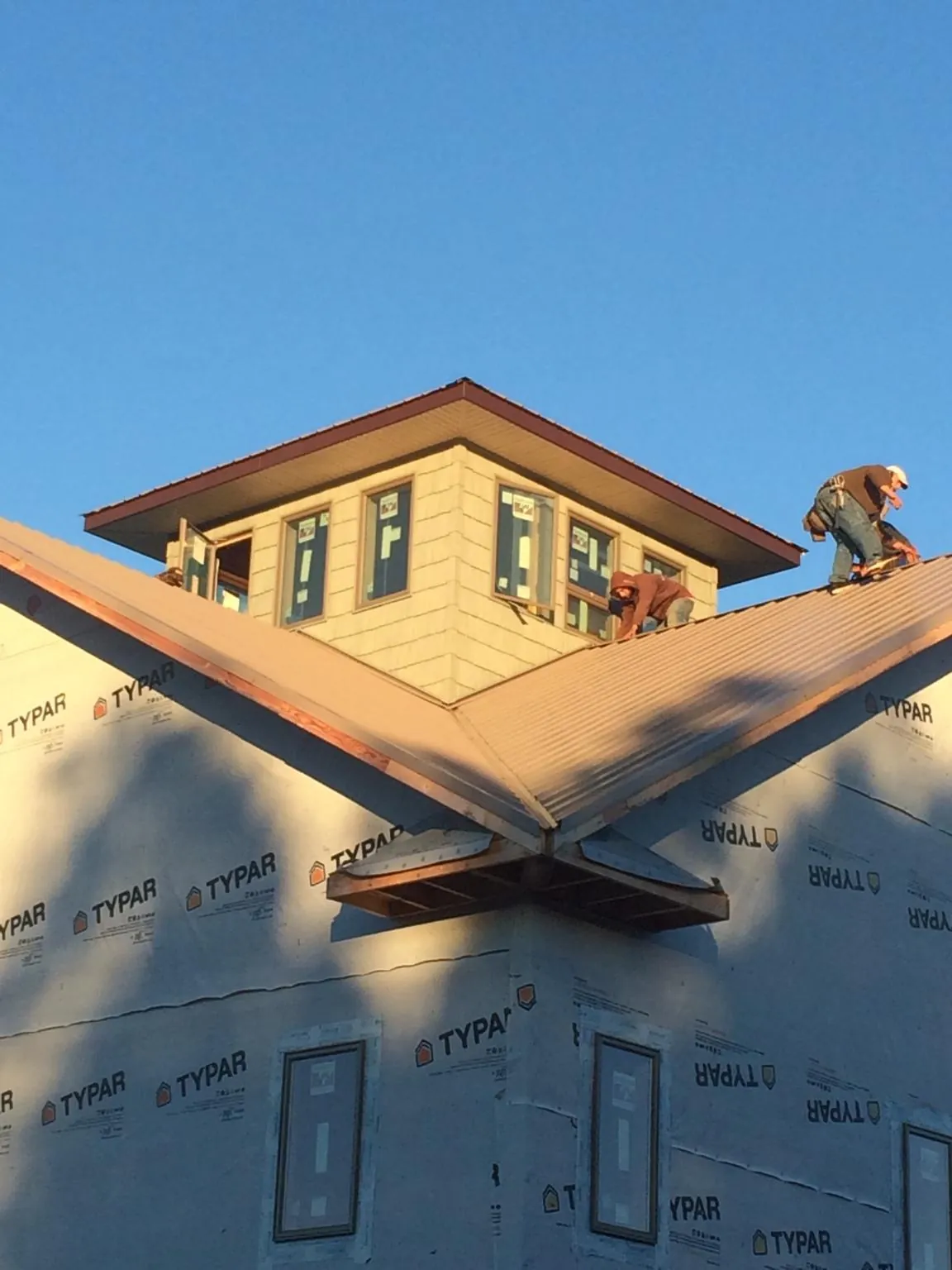 Roofers working around a rooftop cupola on a new metal roof at sunset in East Meadow